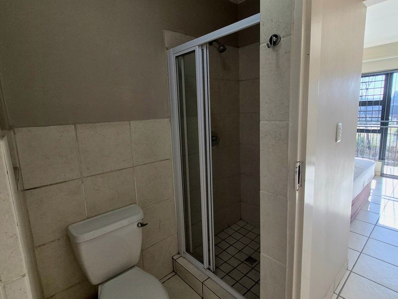 A functional bathroom featuring a shower enclosure and toilet with neutral wall and floor tiling.