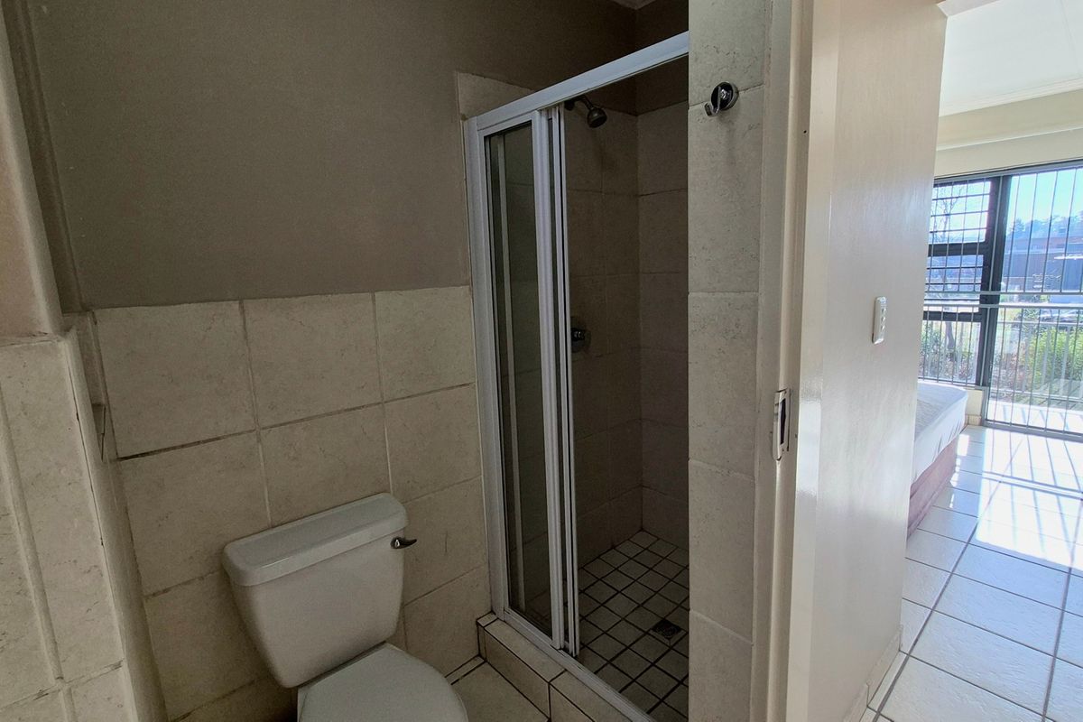 A functional bathroom featuring a shower enclosure and toilet with neutral wall and floor tiling.