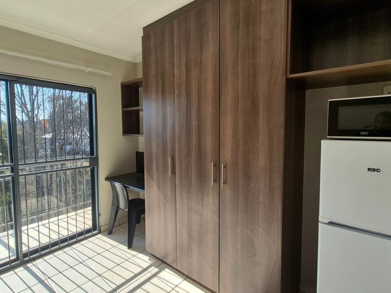 Bedroom featuring built-in wooden cupboards, tiled flooring, and a sliding glass door with security bars leading to an outdoor area.