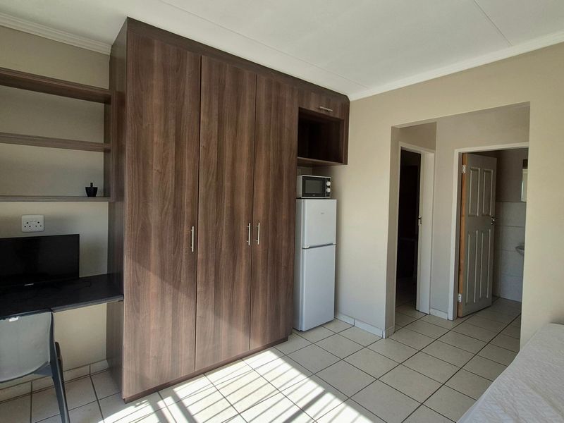 A bedroom featuring built-in wooden cupboards, a fitted desk area, and tiled flooring, providing functional storage and workspace within the apartment.