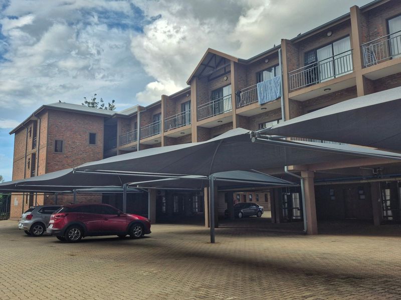 Exterior view of a multi-story apartment complex featuring brick facade, private balconies with metal railings, and covered parking bays.