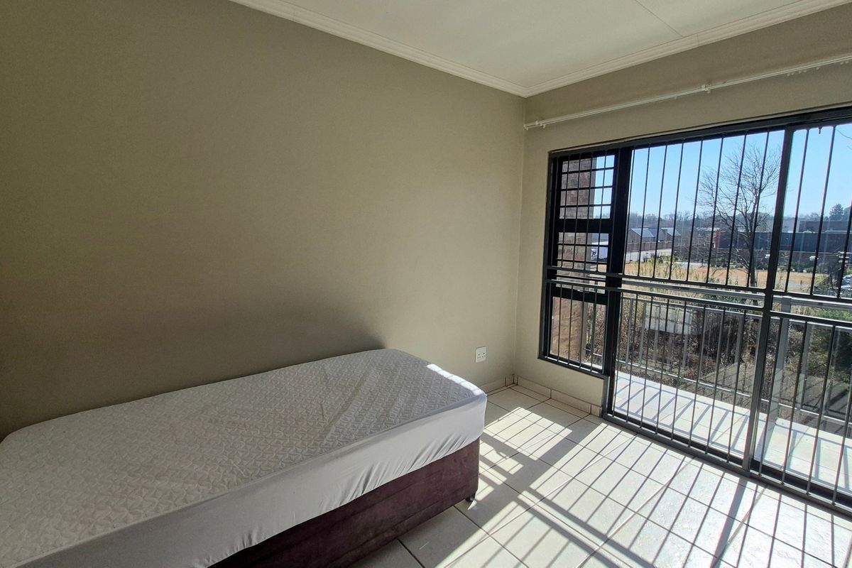 A bedroom featuring tiled flooring and a large sliding glass door with security bars, providing access to an outdoor balcony area.