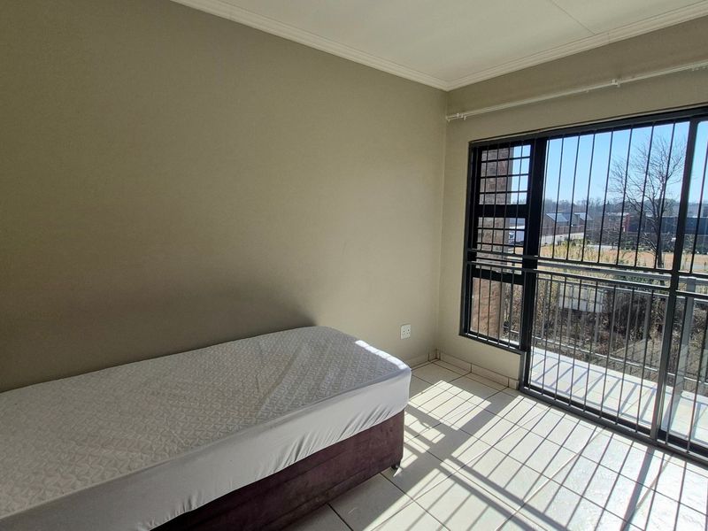 A bedroom featuring tiled flooring and a large sliding glass door with security bars, providing access to an outdoor balcony area.