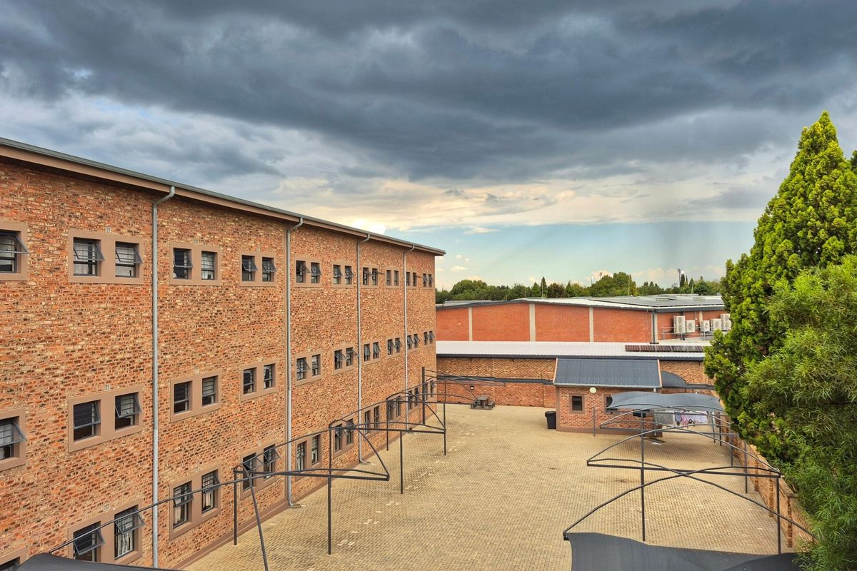 An elevated view of a multi-story face brick apartment building featuring a paved courtyard area with metal carport structures.
