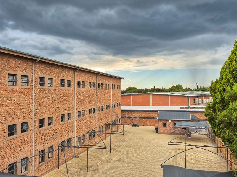 An elevated view of a multi-story face brick apartment building featuring a paved courtyard area with metal carport structures.