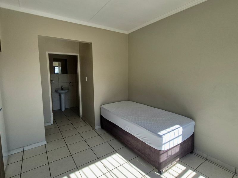 A simple bedroom featuring tiled flooring, a built-in wardrobe, and an adjoining small bathroom area with a pedestal basin.