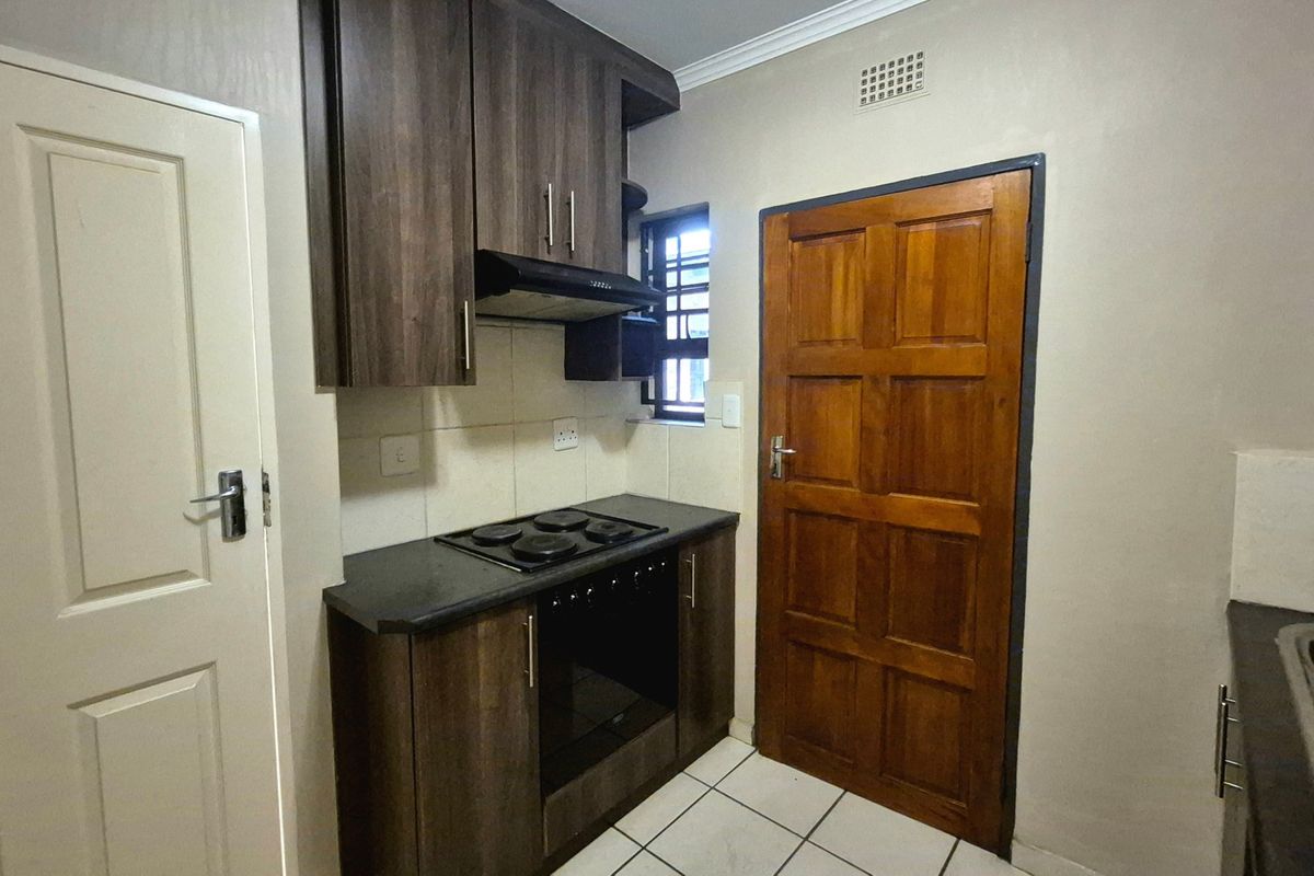 Compact kitchen featuring dark wood cabinetry, built-in oven and hob, extractor fan, and tiled flooring.