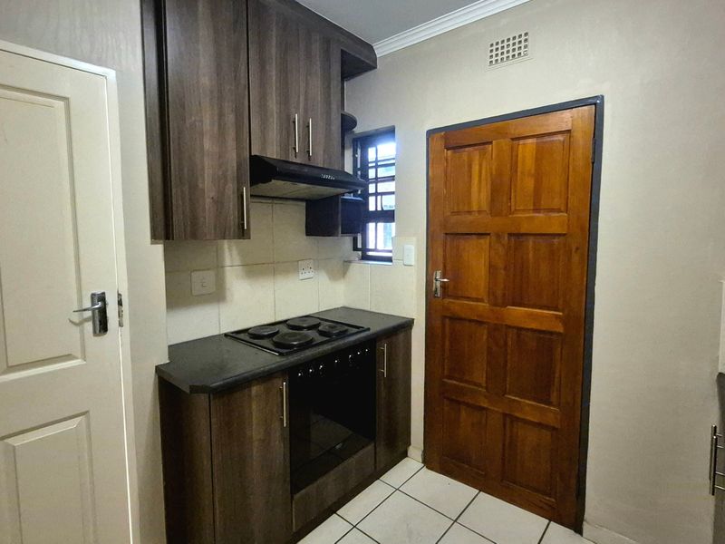 Compact kitchen featuring dark wood cabinetry, built-in oven and hob, extractor fan, and tiled flooring.