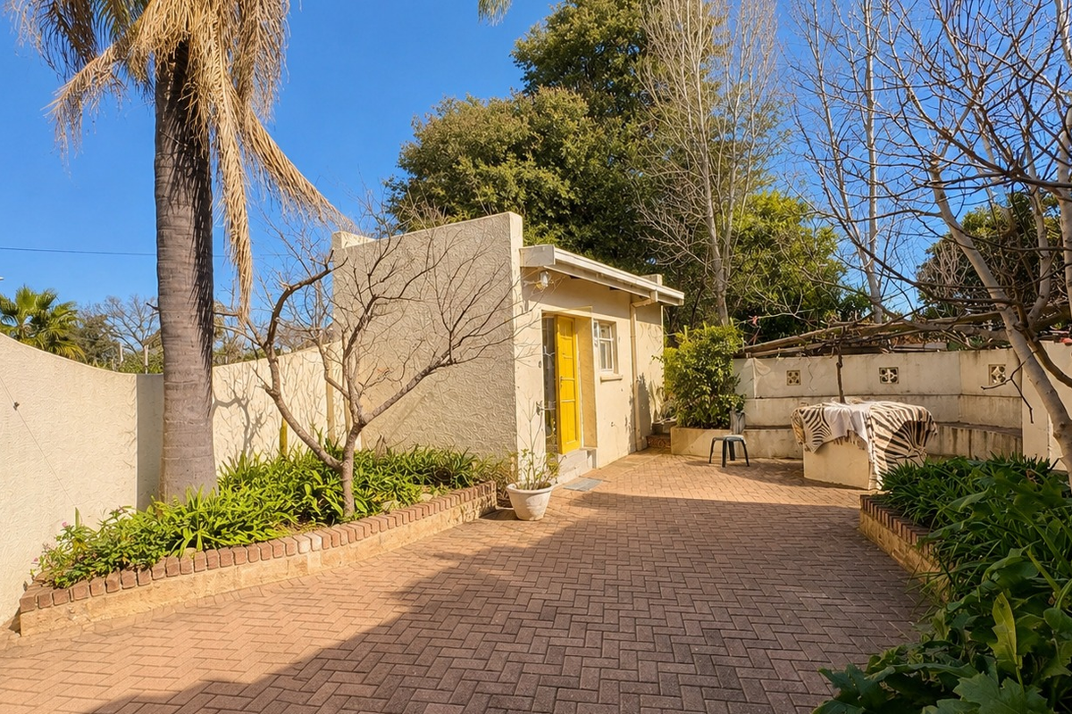 A private rear courtyard featuring paved flooring, built-in seating, and established garden beds with a stucco-finished exterior wall.