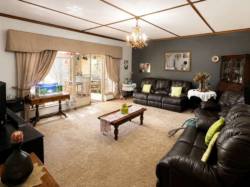 Spacious living room featuring a coffered ceiling, chandelier lighting, and large sliding glass doors providing access to the outdoor patio area.