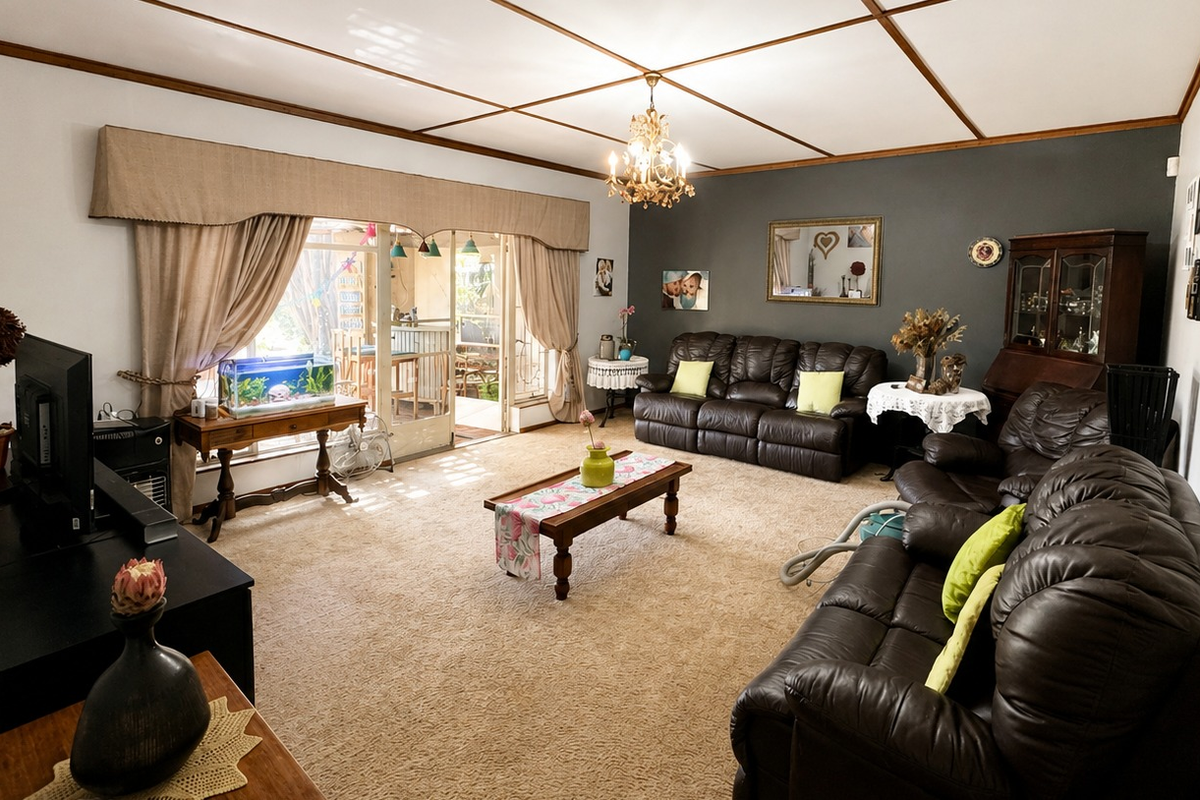 Spacious living room featuring a coffered ceiling, chandelier lighting, and large sliding glass doors providing access to the outdoor patio area.