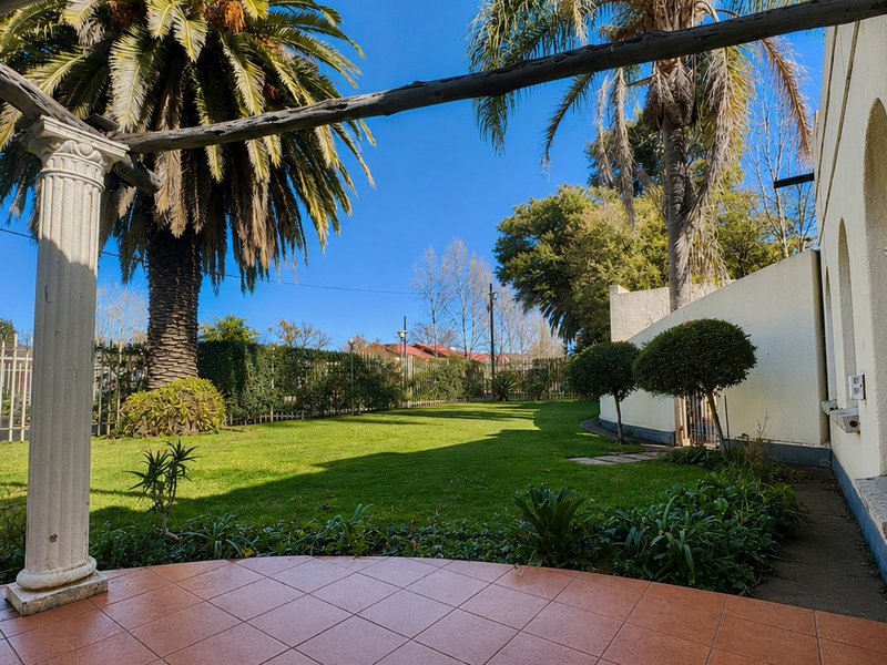 A covered patio area featuring a decorative column and wooden pergola beam, overlooking a spacious, well-maintained garden with mature palm trees.