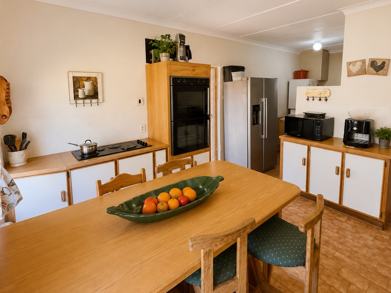 Open plan kitchen and dining area featuring dated timber cabinetry, built-in oven, electric hob, and tiled flooring throughout.
