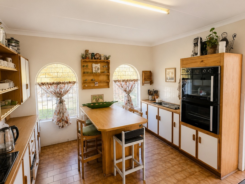 A functional kitchen featuring built-in cabinetry, a double wall oven, electric hob, and arched windows, with direct access to an outdoor patio area.