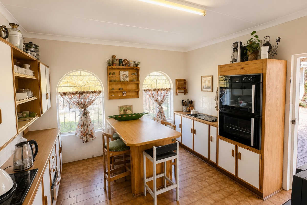 A functional kitchen featuring built-in cabinetry, a double wall oven, electric hob, and arched windows, with direct access to an outdoor patio area.
