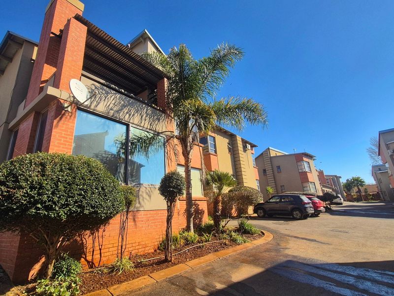 Exterior view of a modern face brick apartment complex featuring a paved driveway, landscaped garden, and private balcony.