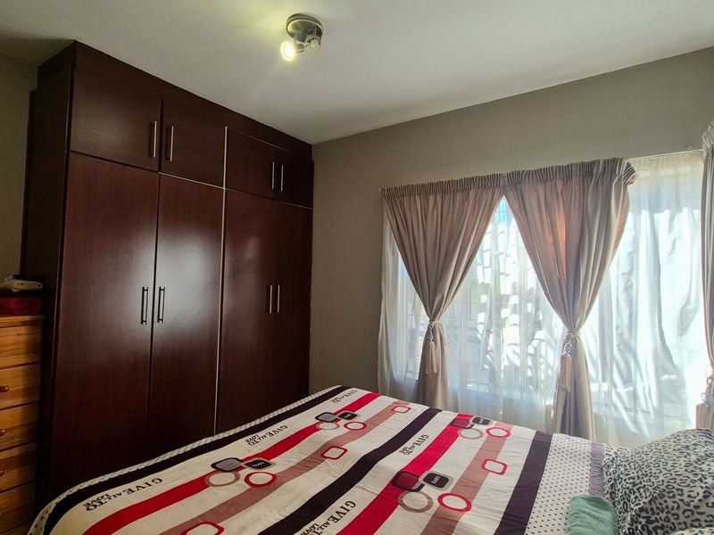 A well-lit bedroom featuring dark wood built-in cupboards and large windows with installed curtain rails.