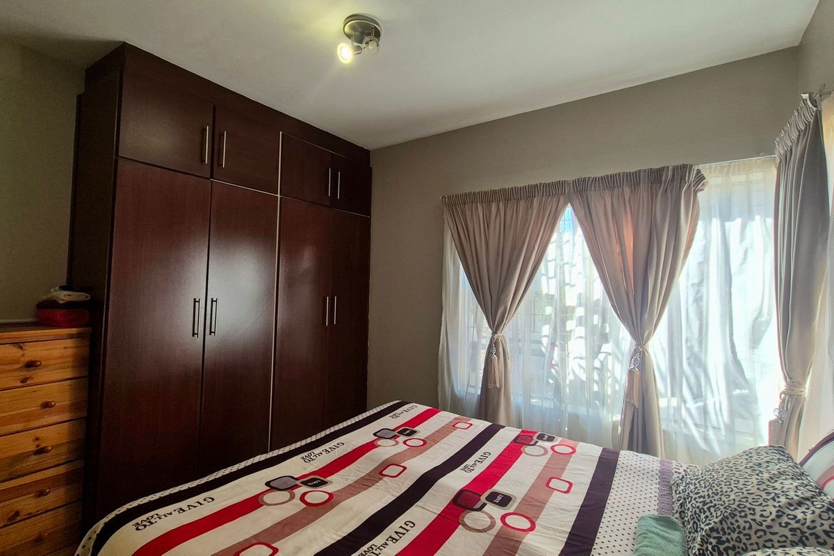 A well-lit bedroom featuring dark wood built-in cupboards and large windows with installed curtain rails.
