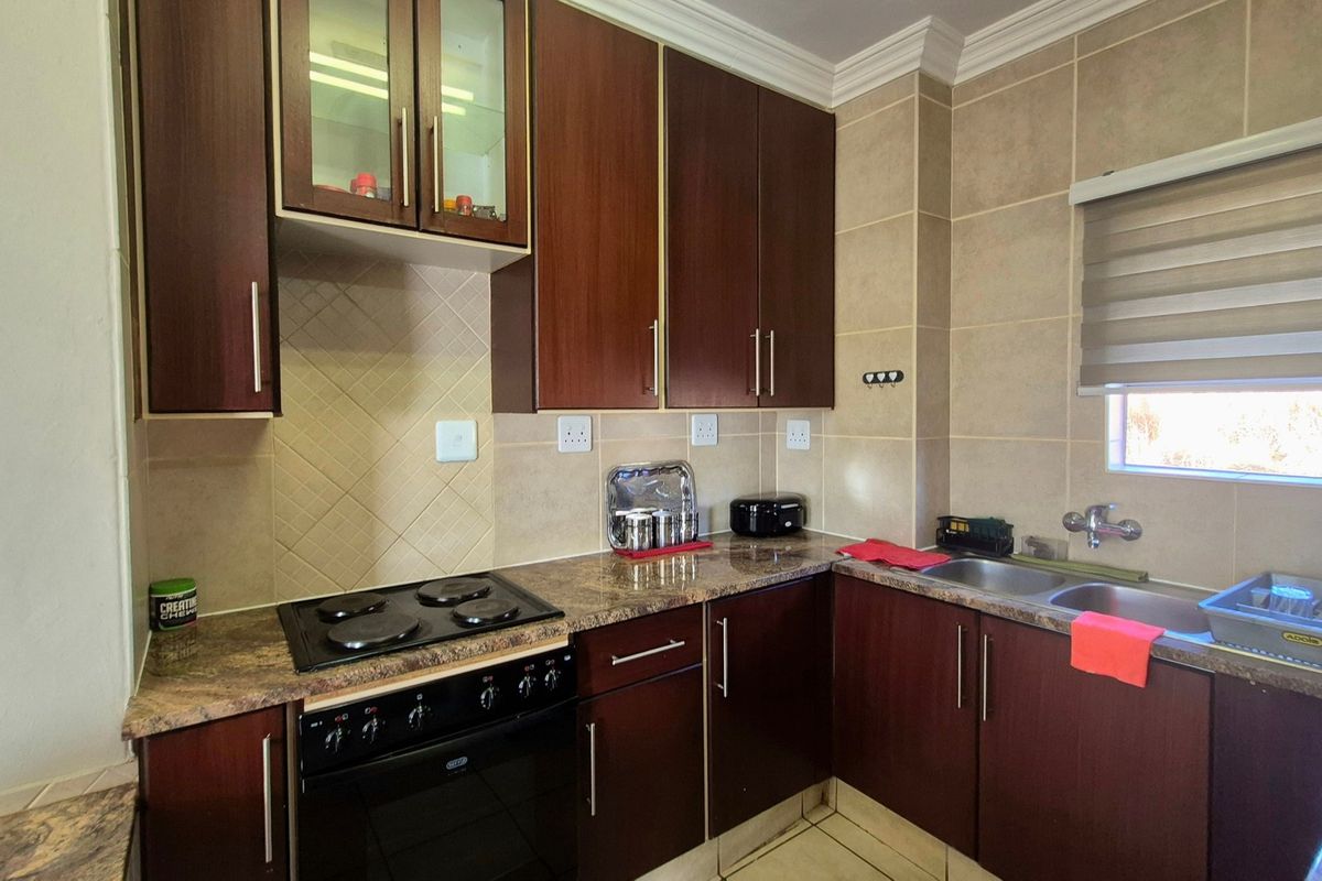 A functional kitchen featuring dark wood cabinetry, granite countertops, a built-in electric hob and oven, and a double basin sink with tiled backsplash.