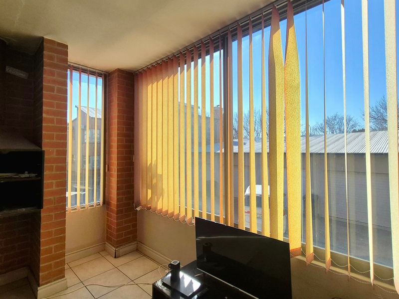 A living area featuring a built-in brick fireplace, tiled flooring, and large windows with vertical blinds, offering a functional space with potential for modernization.