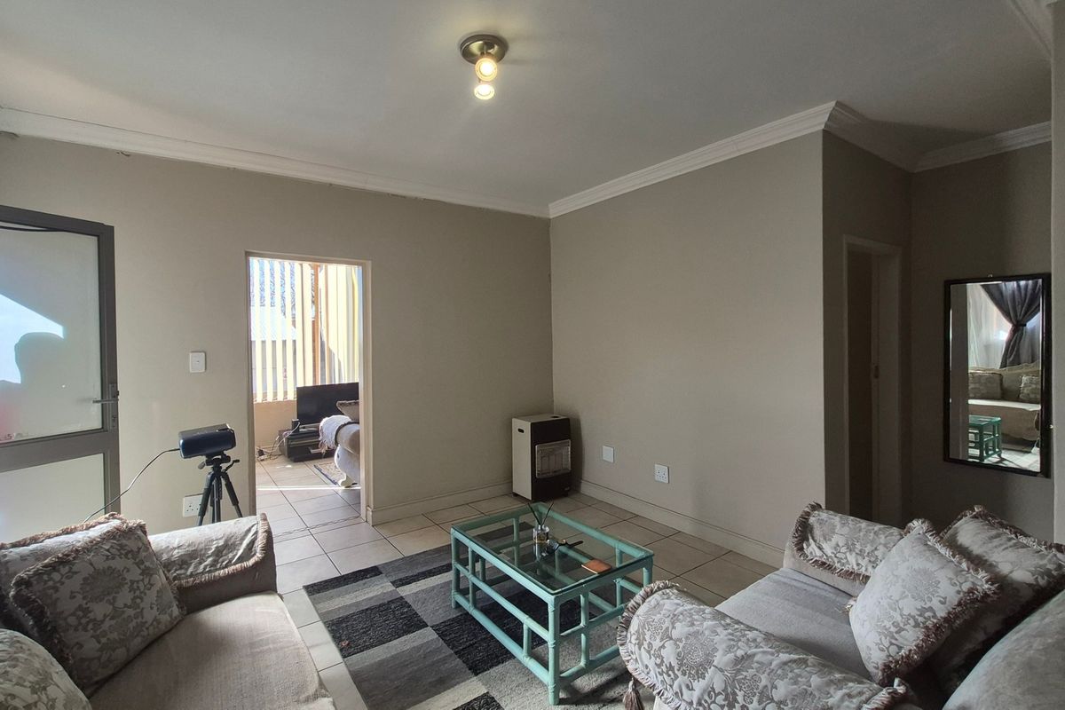 A living room area featuring tiled flooring, neutral wall tones, and ceiling cornice detailing, with an adjacent room visible through the doorway.