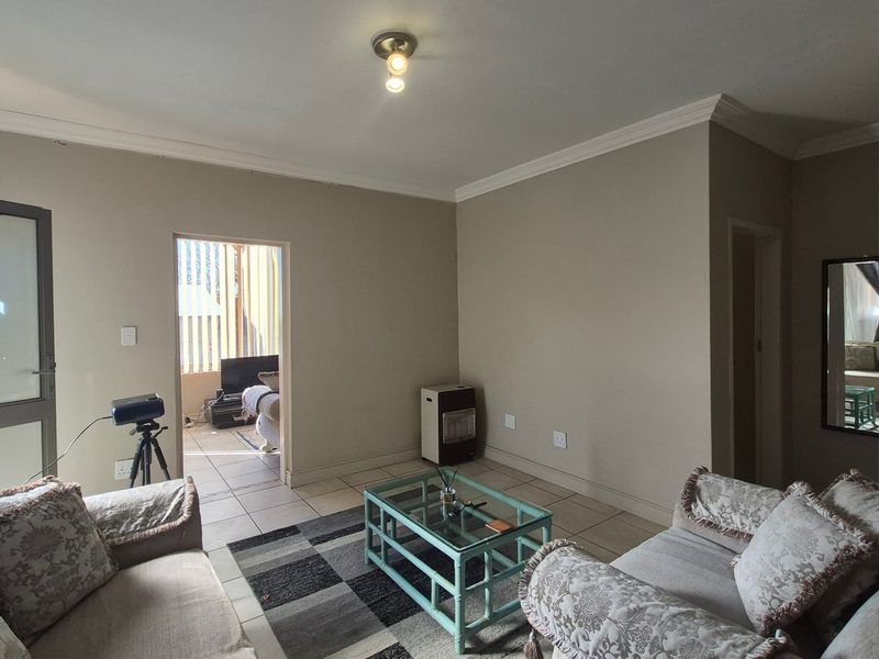 A living room area featuring tiled flooring, neutral wall tones, and ceiling cornice detailing, with an adjacent room visible through the doorway.