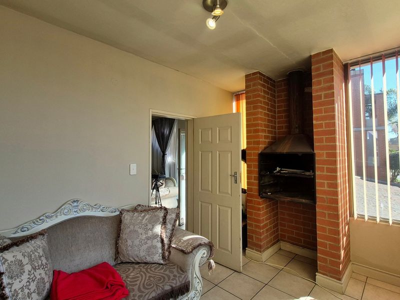Living area featuring a built-in brick fireplace, tiled flooring, and large windows with vertical blinds, offering a cozy and functional space.