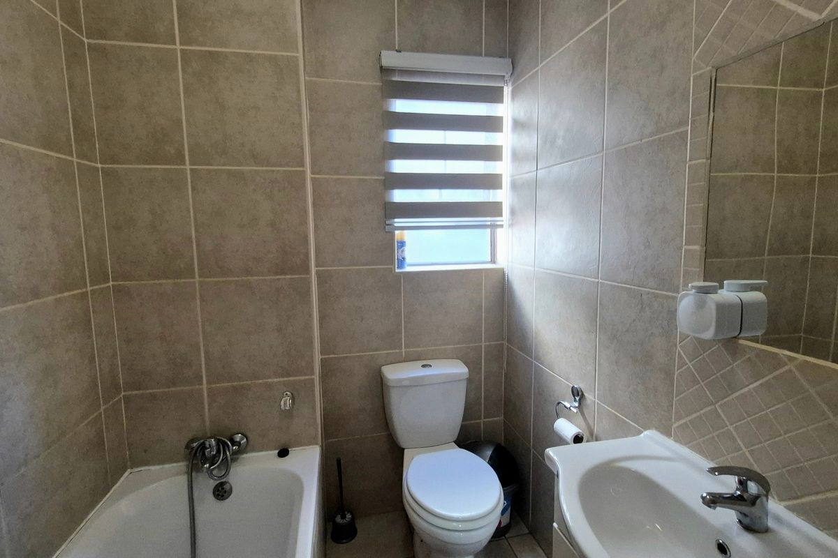 A functional bathroom featuring full-height wall tiling, a bathtub with shower mixer, a pedestal basin, and a toilet.