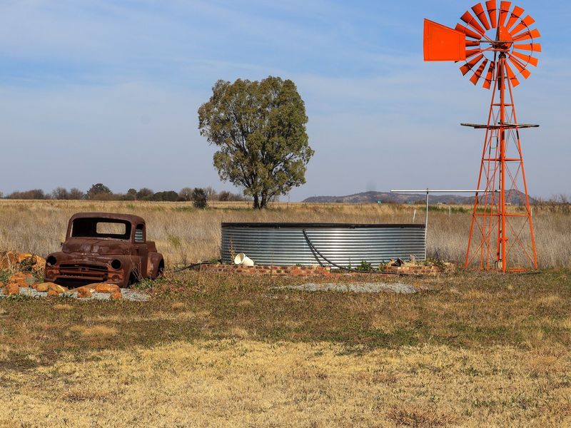 Open rural landscape featuring a traditional orange windmill and a corrugated steel water tank on the small holding property.