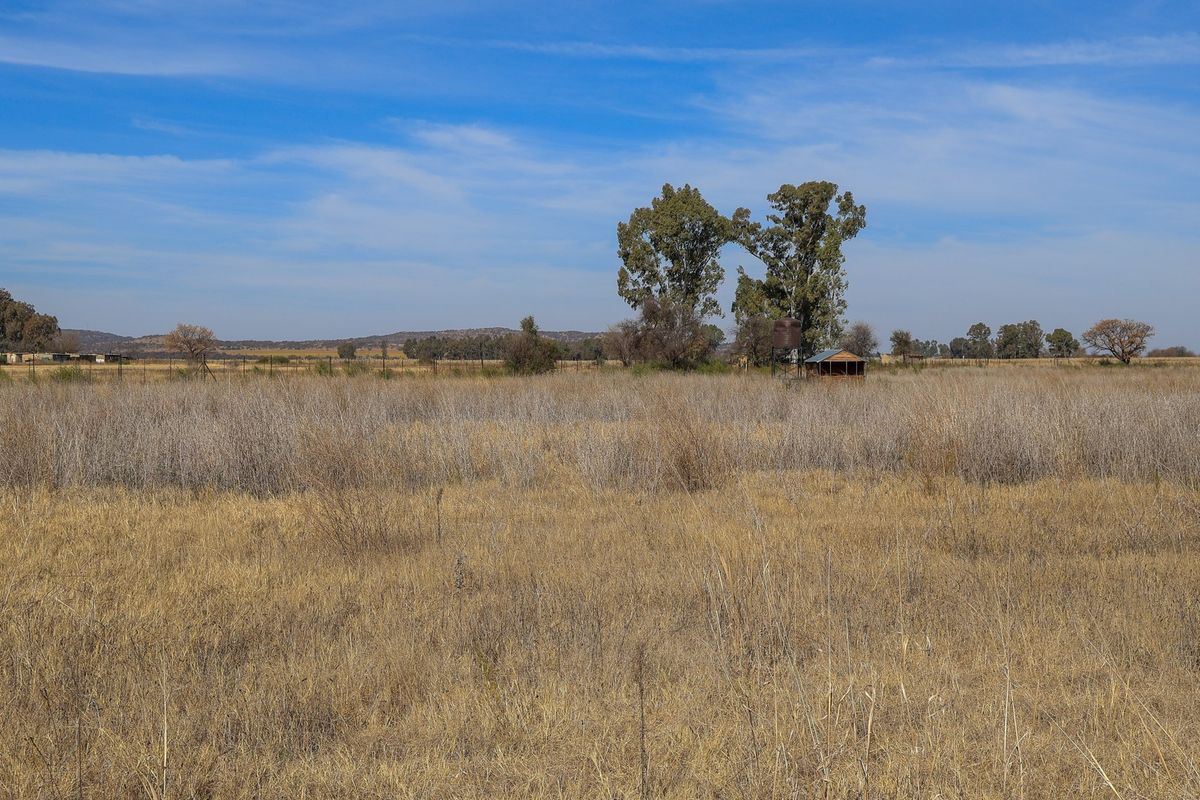 Expansive open field on a small holding, featuring natural dry vegetation, perimeter fencing, and a small utility structure with a water tank.