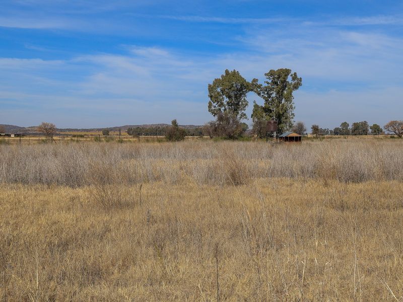 Expansive open field on a small holding, featuring natural dry vegetation, perimeter fencing, and a small utility structure with a water tank.