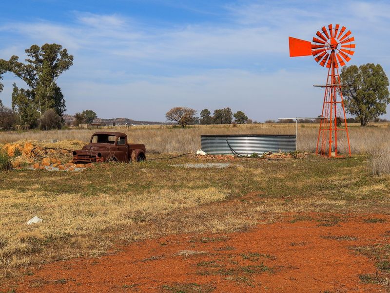 Open small holding landscape featuring a traditional red windmill and a corrugated steel water storage tank set in a rural field.