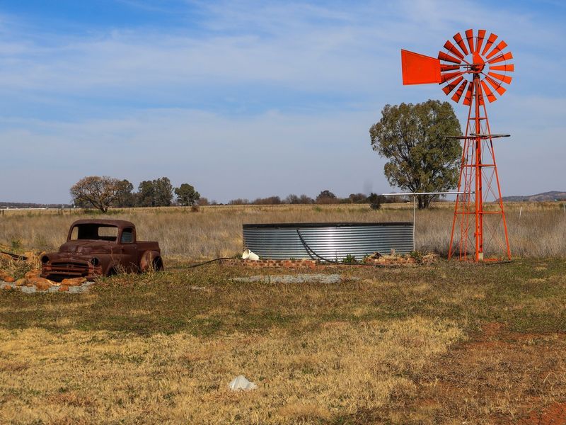Outdoor area featuring a traditional metal windmill and a corrugated steel water tank set within a large, open rural landscape.