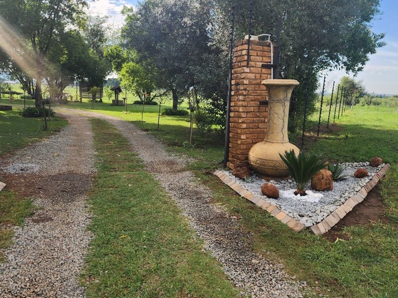 Entrance to the small holding featuring brick gate pillars, a gravel driveway, and well-maintained garden landscaping with electric fencing.
