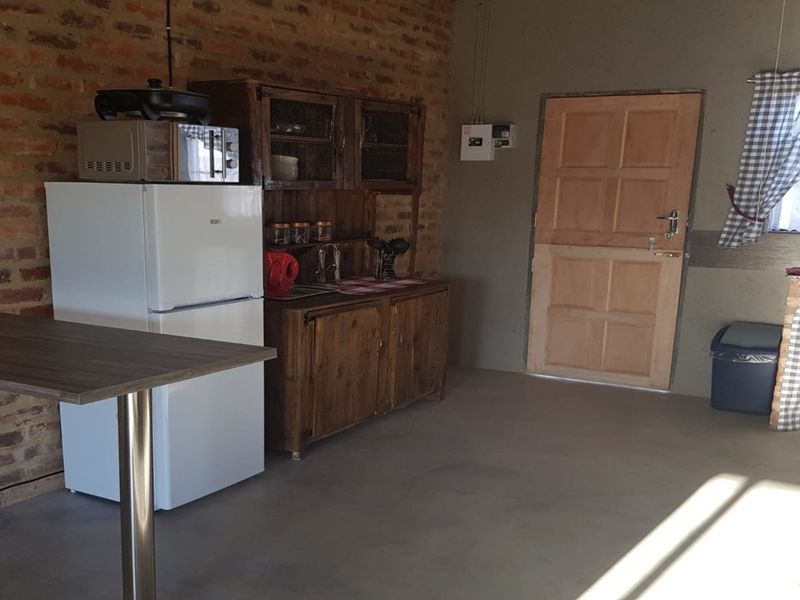 A rustic kitchen area featuring exposed brick walls, concrete flooring, and wooden cabinetry, providing a functional but dated utility space.