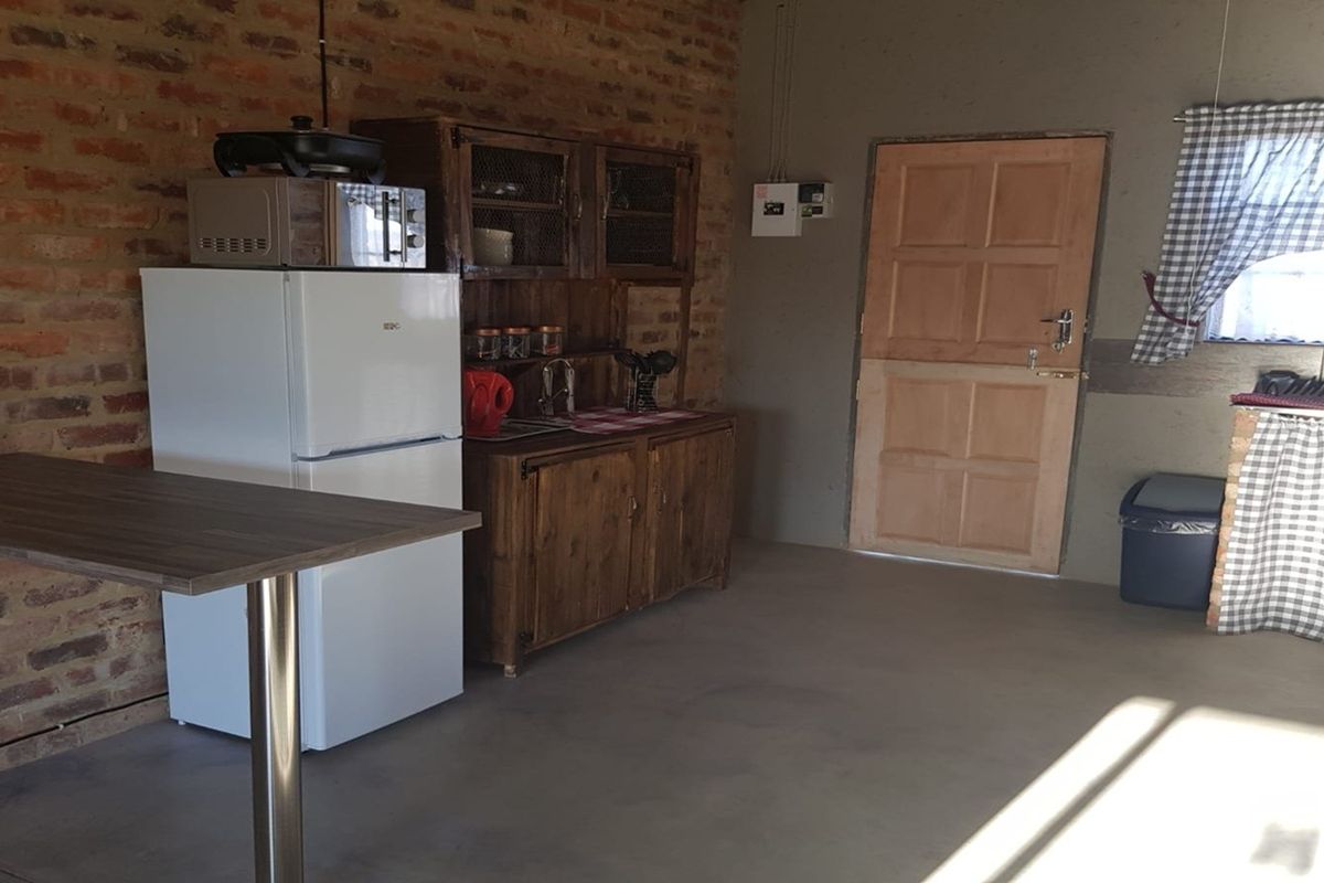 A rustic kitchen area featuring exposed brick walls, concrete flooring, and wooden cabinetry, providing a functional but dated utility space.