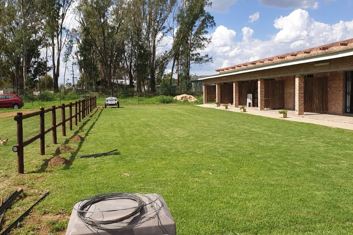 A spacious rear garden featuring a well-maintained lawn, a covered brick patio area, and timber post-and-rail fencing on a small holding property.