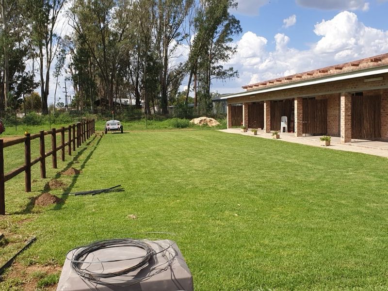 A spacious rear garden featuring a well-maintained lawn, a covered brick patio area, and timber post-and-rail fencing on a small holding property.