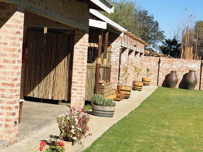 A covered outdoor patio area featuring exposed brick pillars and concrete flooring, overlooking a well-maintained garden with a brick boundary wall.
