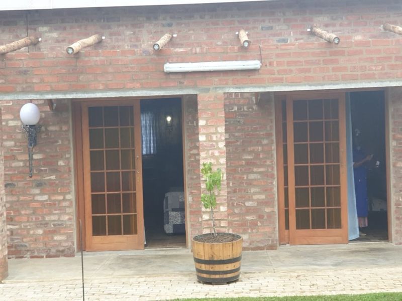 A covered patio area featuring exposed brickwork, timber rafter detailing, and double wooden french doors providing access to the interior.