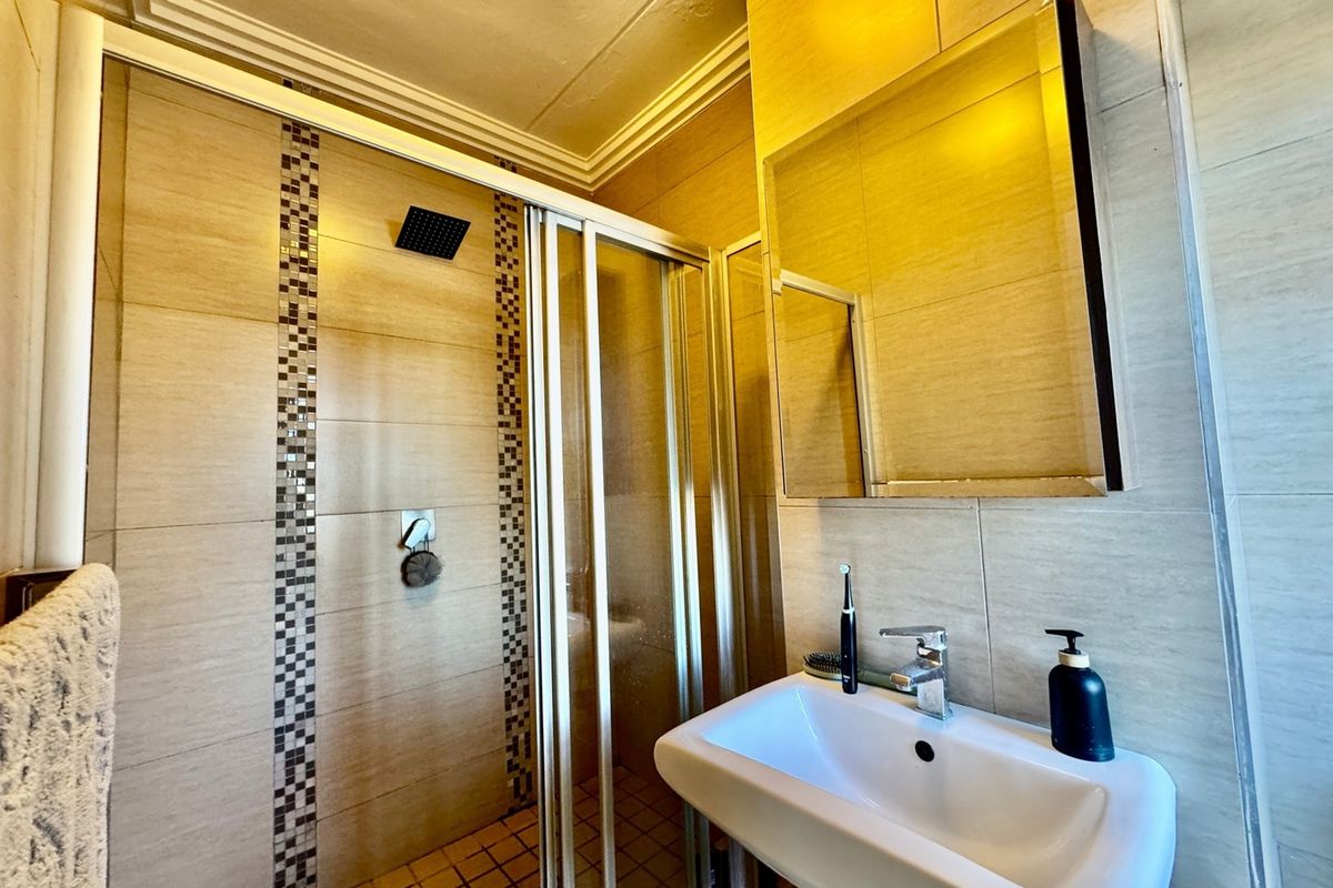 A compact bathroom featuring a shower enclosure with a rain shower head, a wall-mounted basin, and a mirrored medicine cabinet with tiled finishes.