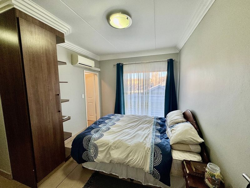 A functional bedroom featuring tiled flooring, crown molding, a built-in wardrobe, and a wall-mounted air conditioning unit.