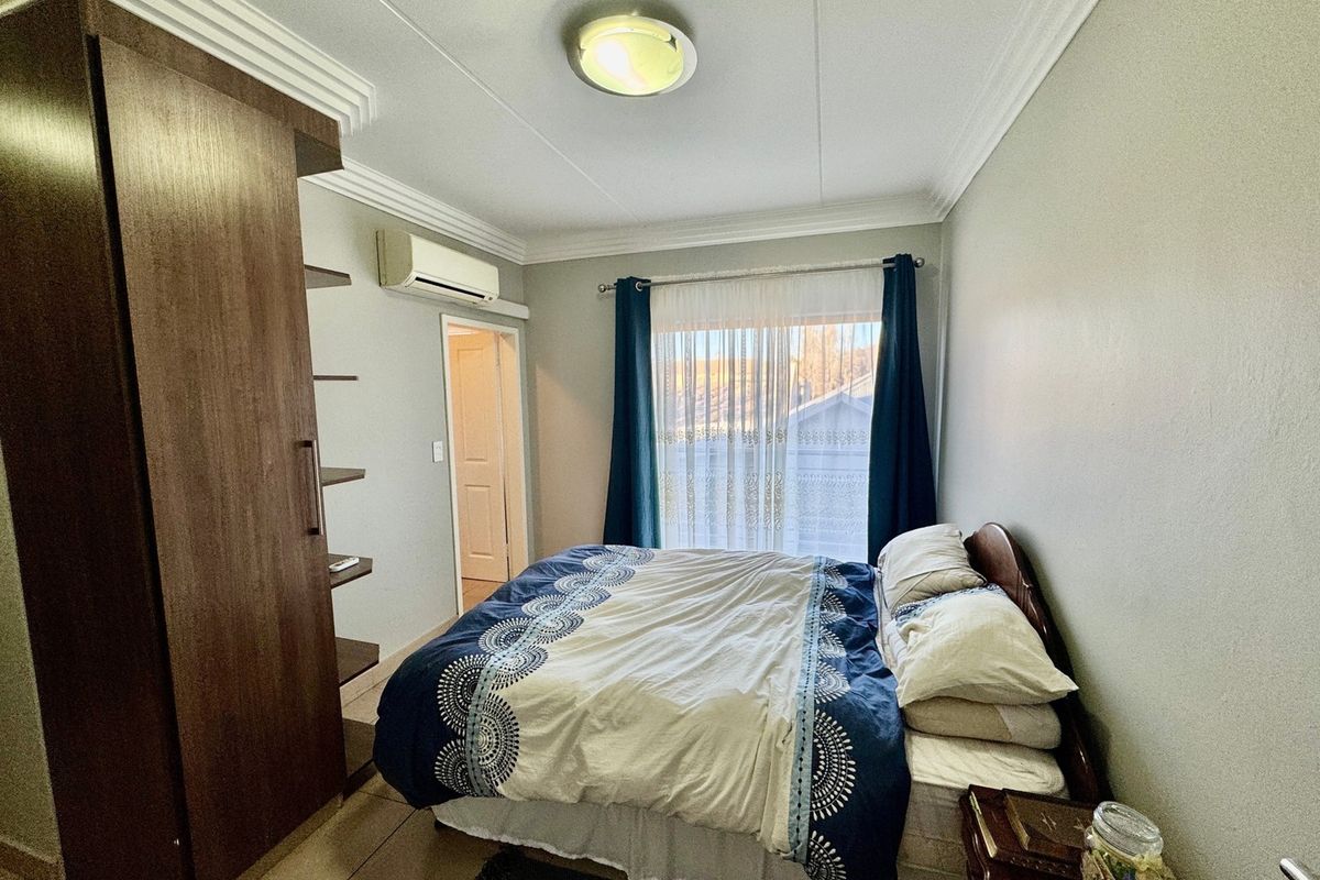 A functional bedroom featuring tiled flooring, crown molding, a built-in wardrobe, and a wall-mounted air conditioning unit.