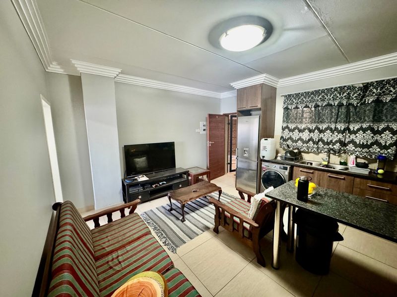 Open-plan living area featuring a compact kitchen with granite countertops, built-in cabinetry, and tiled flooring throughout the combined space.
