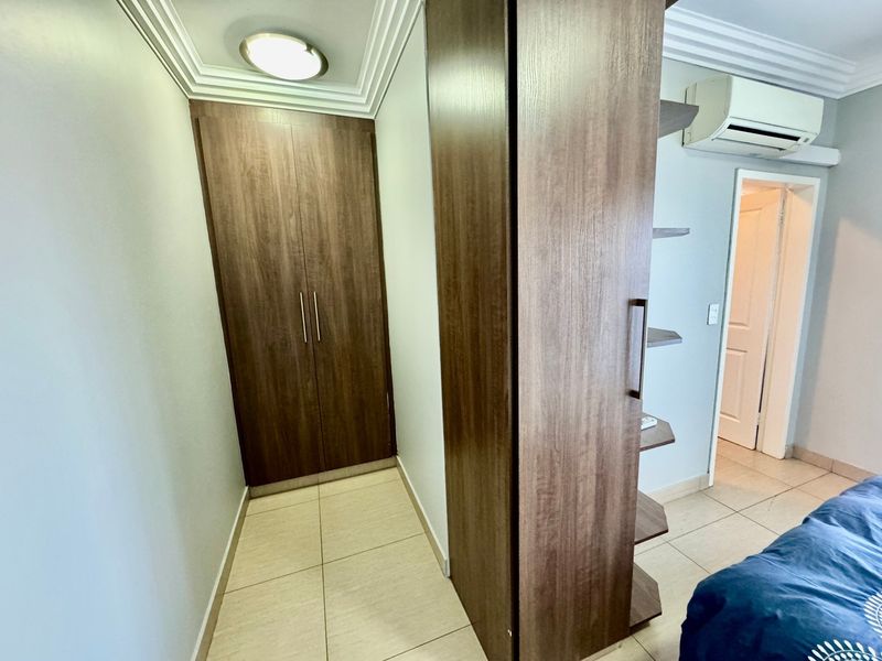 A bedroom featuring built-in wooden cupboards, tiled flooring, crown molding, and a wall-mounted split-system air conditioning unit.