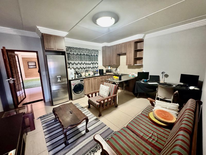 Open-plan living area featuring a functional kitchen with built-in cabinetry, tiled flooring, and integrated appliances, seamlessly connecting to the lounge space.