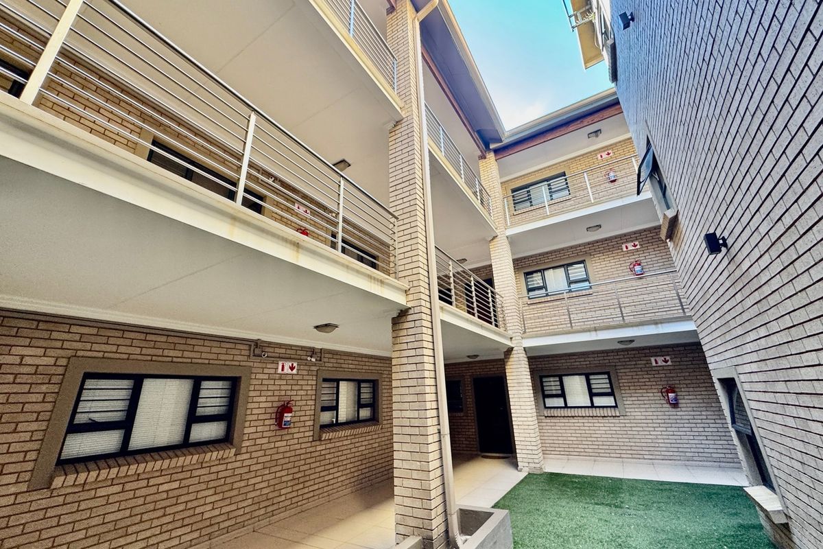 Exterior view of an apartment complex featuring face brick facade, multi-level walkways with stainless steel balustrades, and a small ground-level courtyard area.