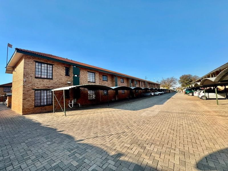 Exterior view of a multi-story apartment complex featuring face brick construction, a paved driveway, and dedicated covered carport parking bays.