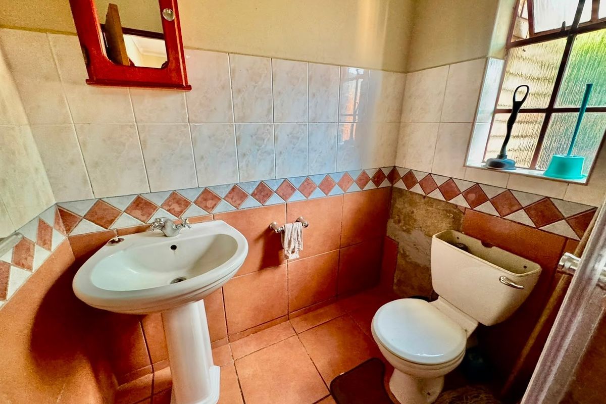 A compact bathroom featuring a pedestal basin and toilet, with dated wall tiling and visible damage to the wall surface requiring repair.