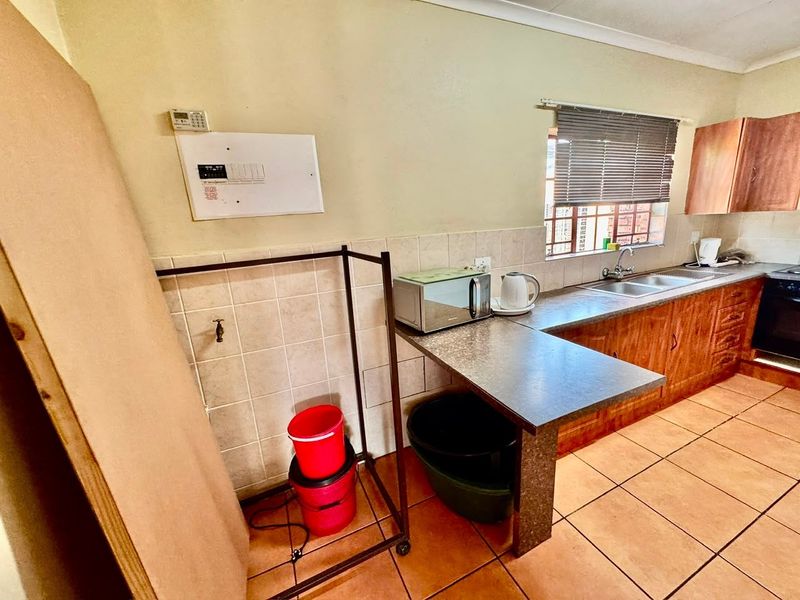 A functional kitchen featuring laminate countertops, a double basin sink, tiled backsplash, and built-in cabinetry with ceramic floor tiles.